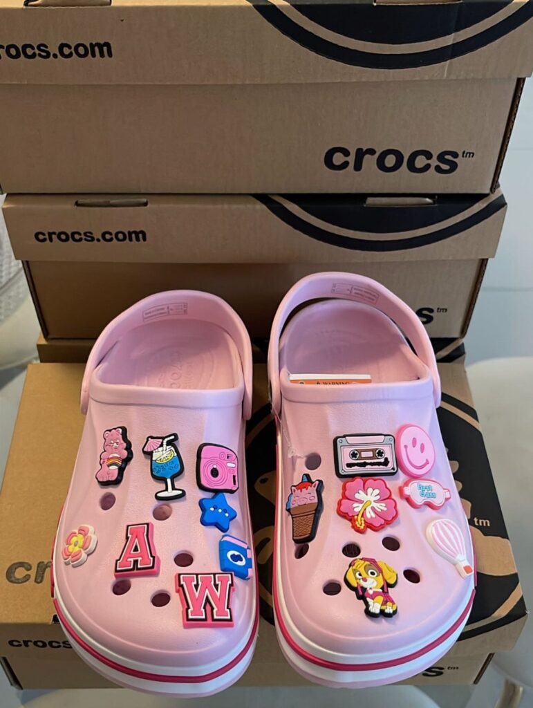 Pink Crocs clogs with colorful charms placed in front of branded shoe boxes.