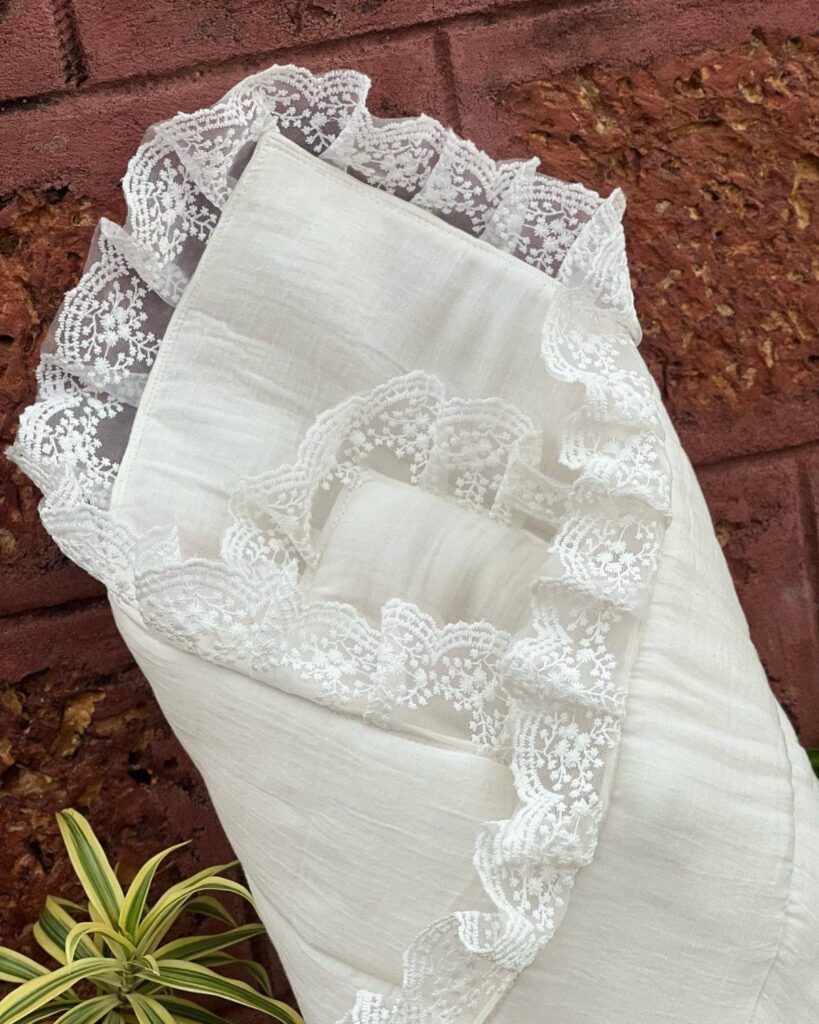 White lace swaddle blanket wrapped and leaning against a red brick wall.