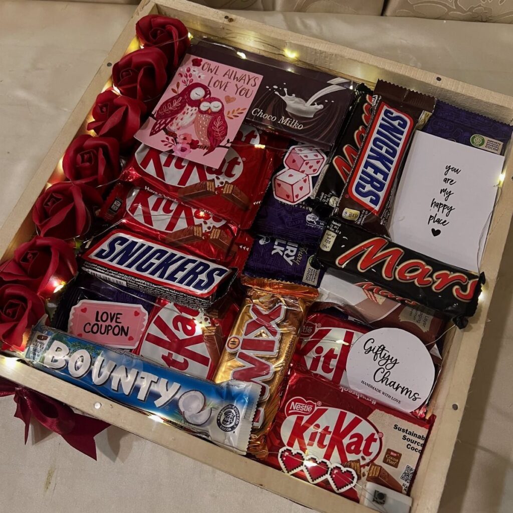 Wooden gift box filled with assorted chocolate bars, red roses, and love notes.