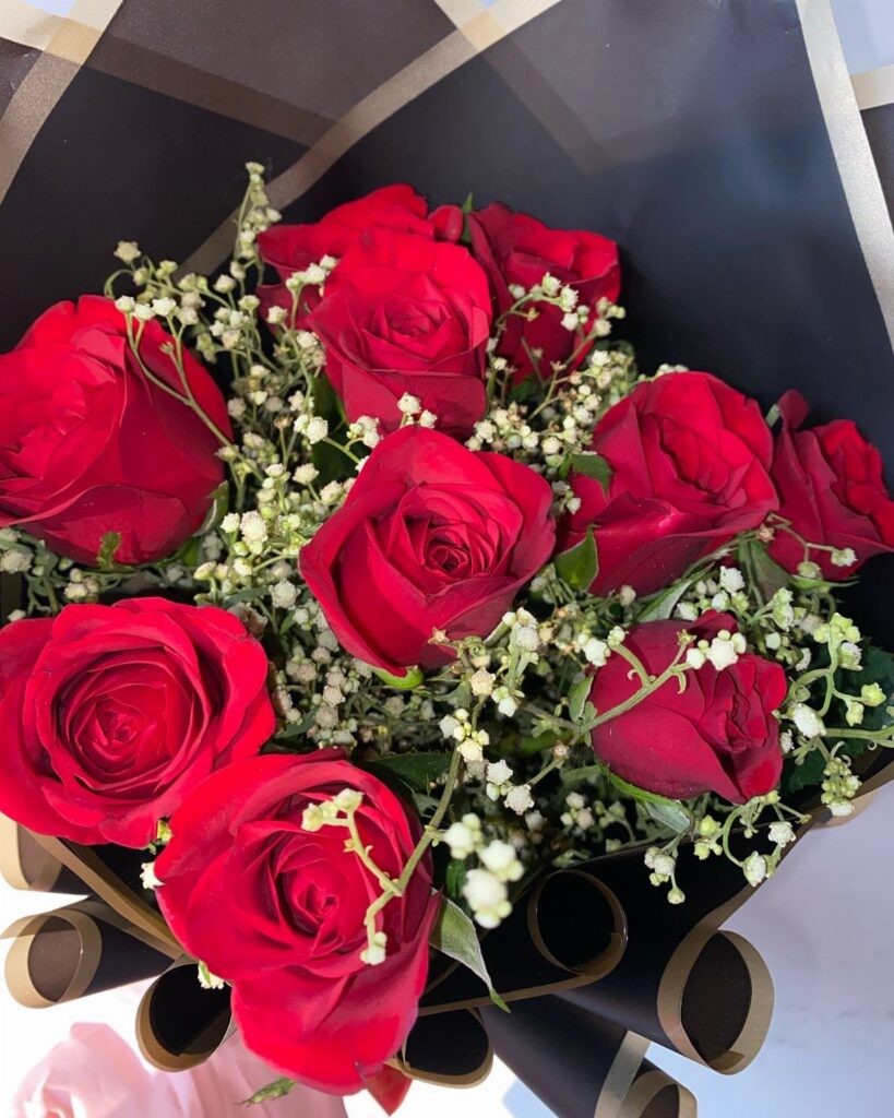 Red roses and white baby's breath wrapped in black and gold paper.