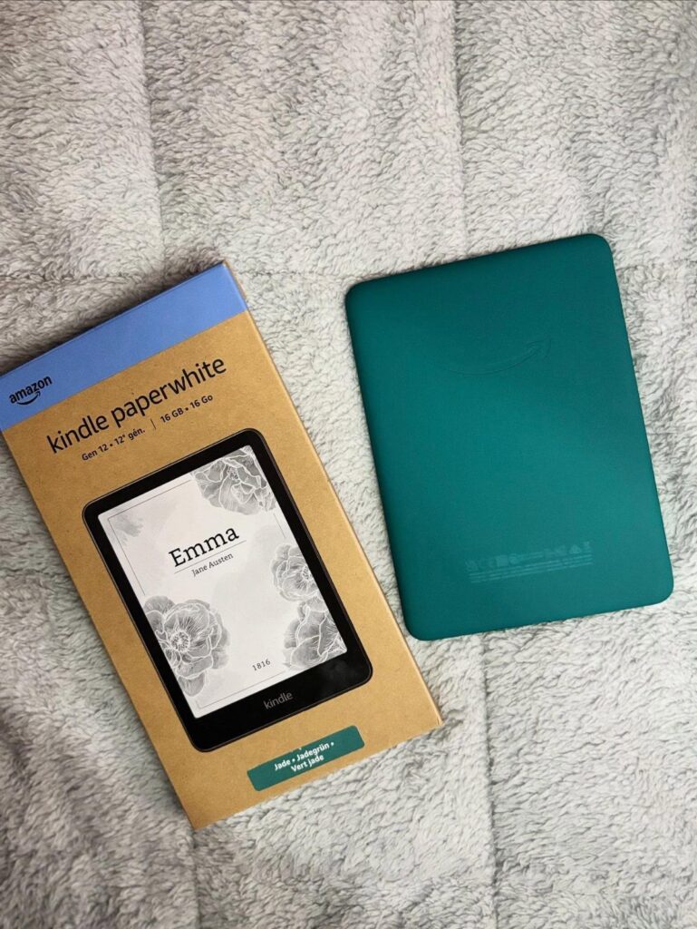 Teal Amazon Kindle Paperwhite e-reader next to its original cardboard packaging box.
