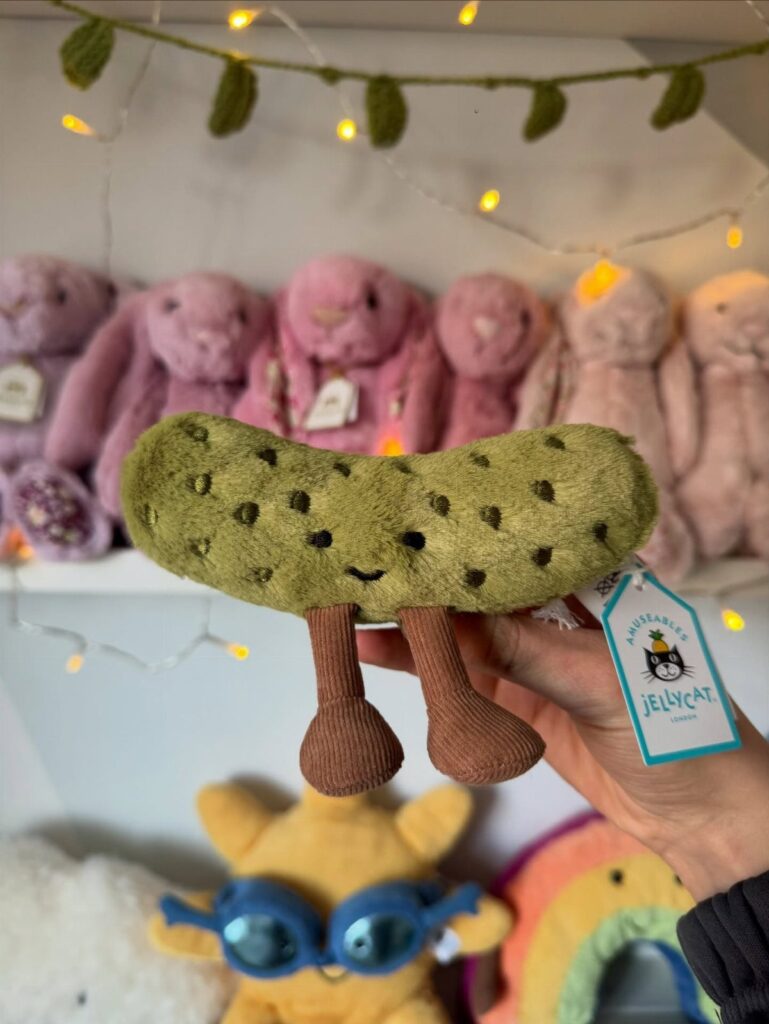 Green plush pickle toy with brown legs held in front of pink bunnies.