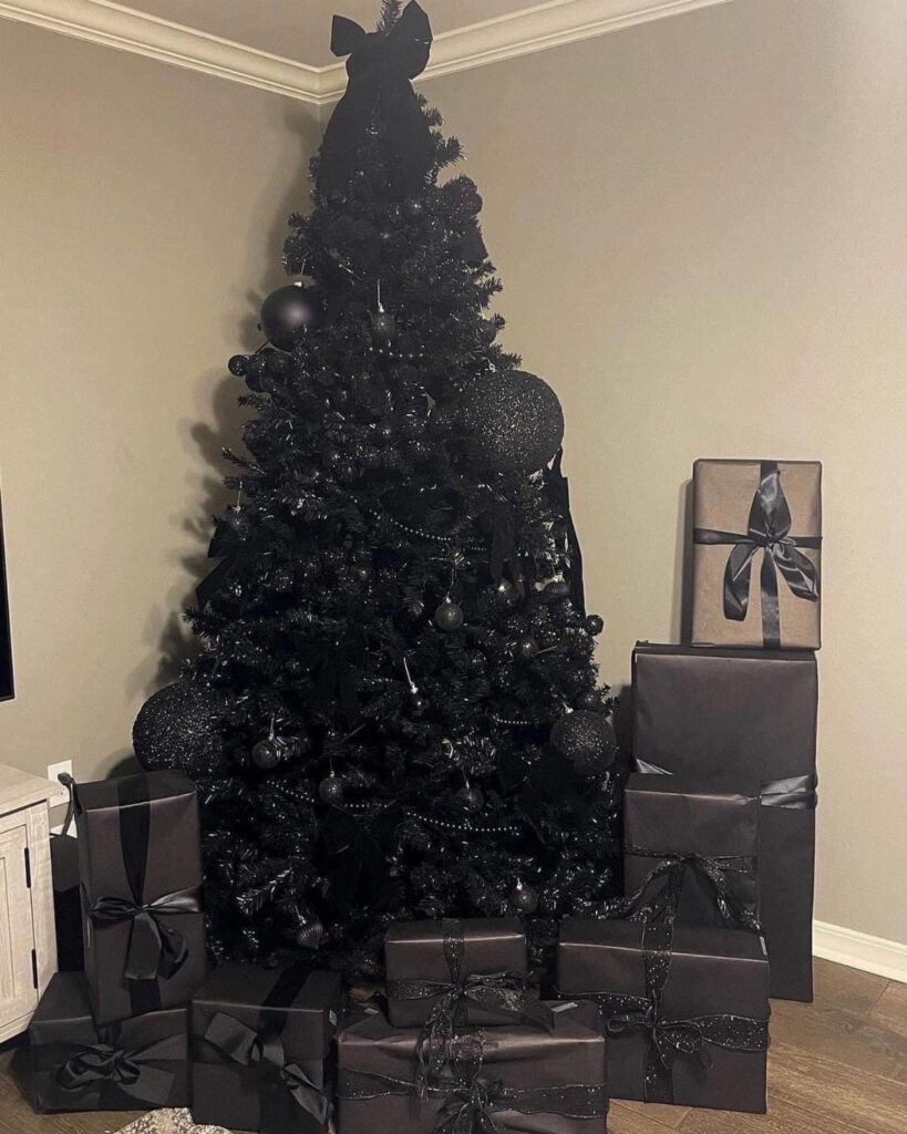 Black Christmas tree with black ornaments and matching wrapped gifts against a grey wall
