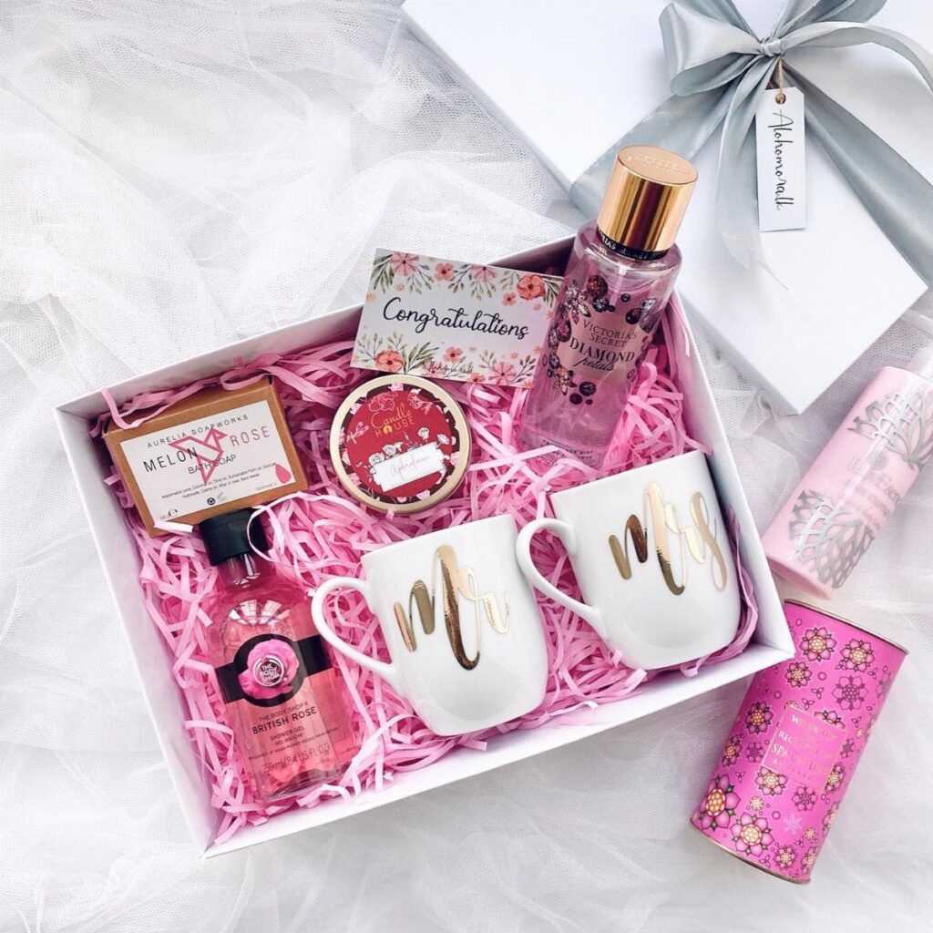 Bridal shower gift box with pink perfume, gold lettered mugs, and a card.