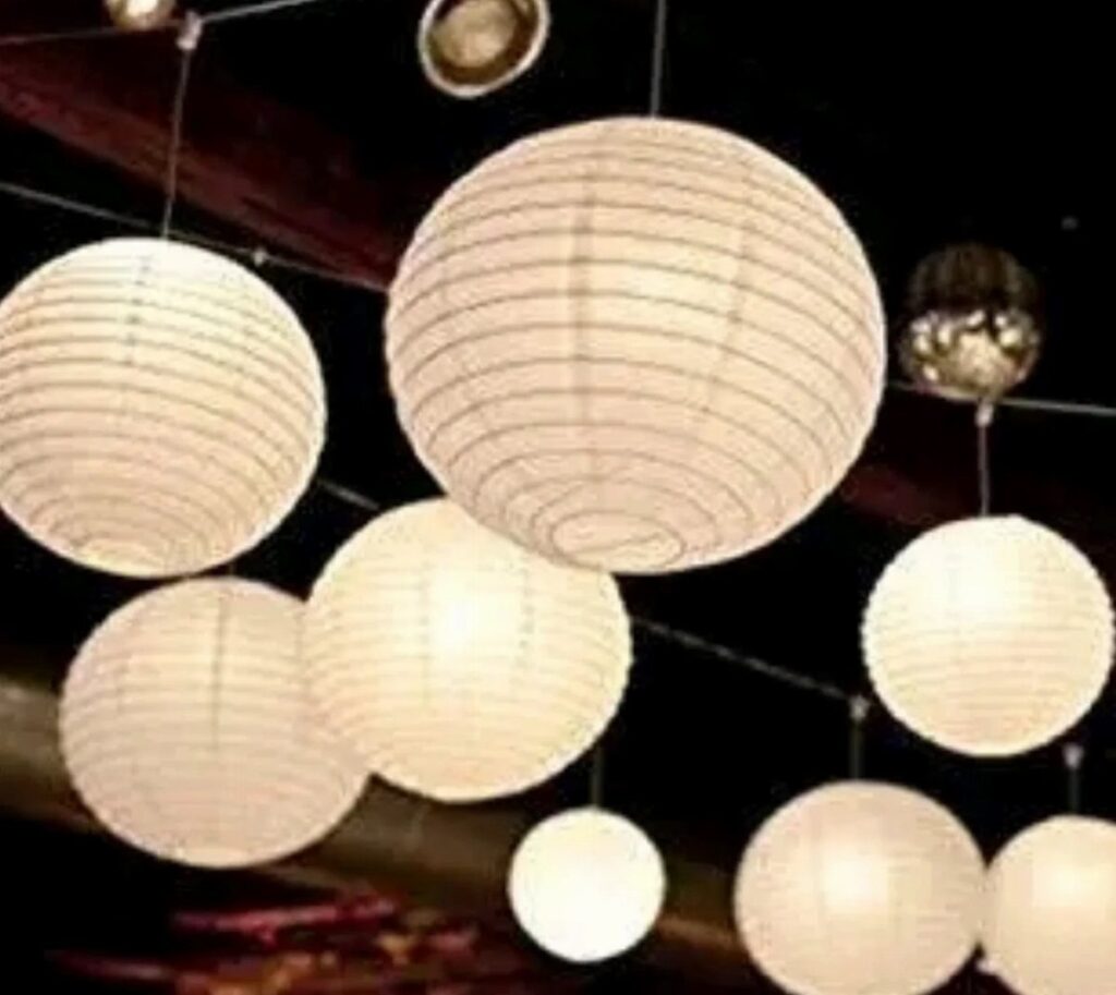 White spherical paper lanterns glowing with warm light hanging from a dark ceiling.