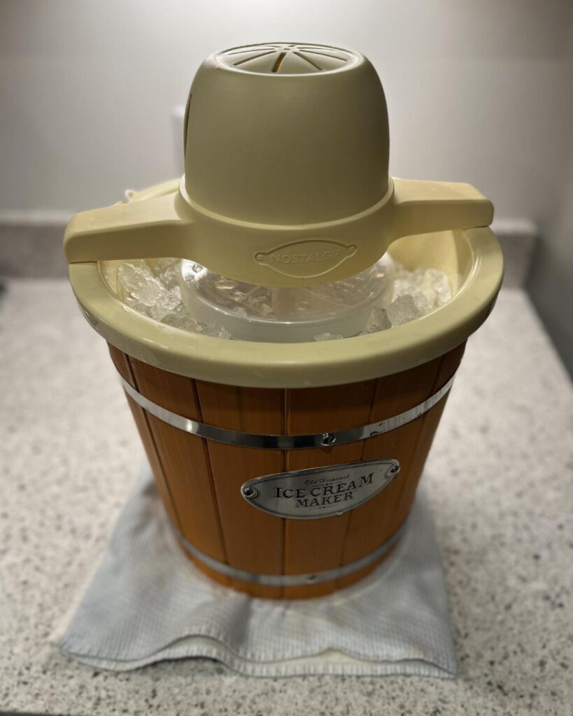 Vintage-style ice cream maker with wooden barrel base and ice on a counter