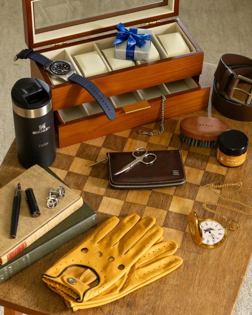 Men's accessories including leather gloves, watch box, and travel mug on a chessboard table