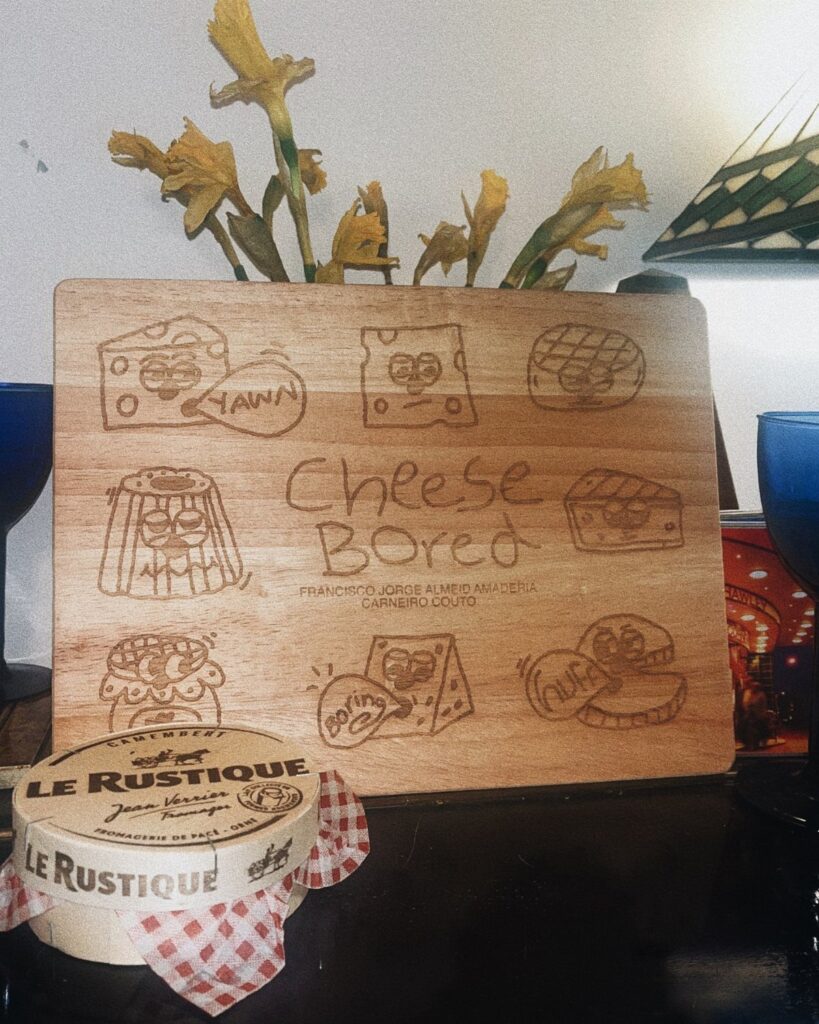 Engraved wooden cheese board with cartoon illustrations and a wheel of brie cheese.