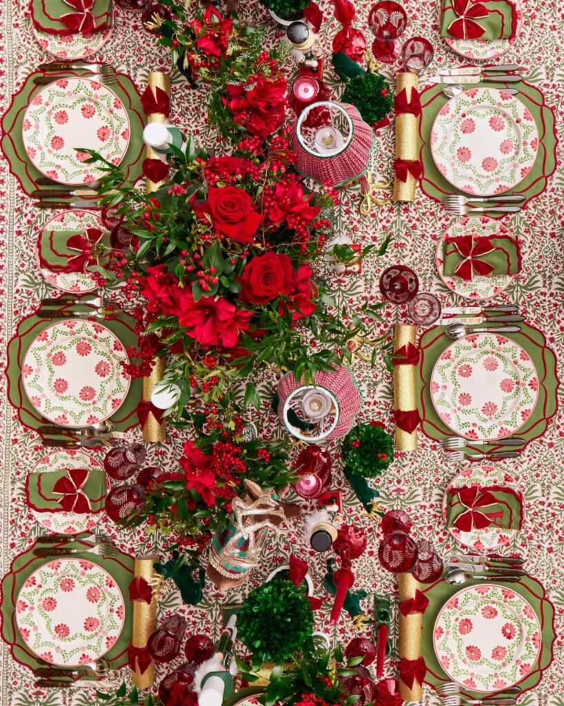 Festive Christmas table setting with red roses, patterned plates, and gold accents.