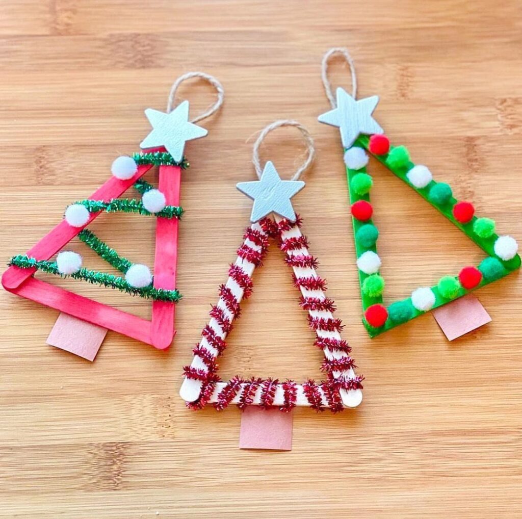 Three popsicle stick Christmas tree ornaments decorated with pom poms and tinsel.