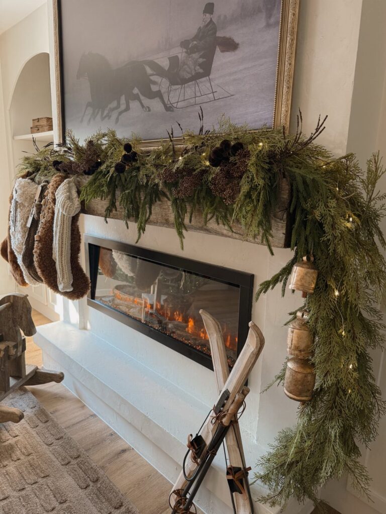 Rustic wooden mantel decorated with green pine garland, twinkle lights, and hanging stockings.