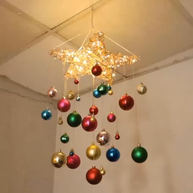 Star-shaped light fixture decorated with colorful hanging Christmas ornaments in a room.