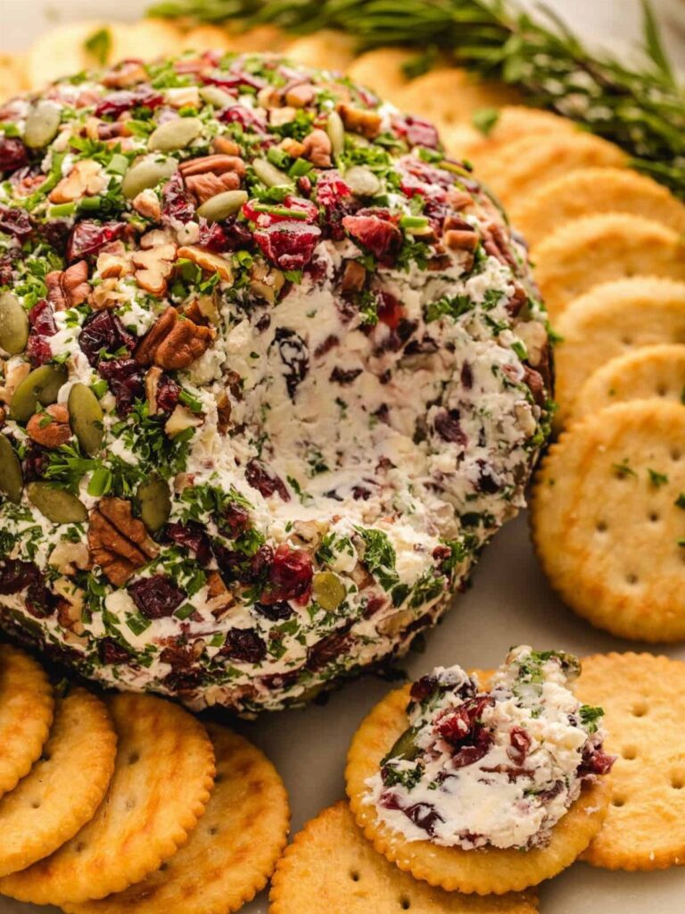 Cranberry-pecan cheese ball with herbs served with round crackers and fresh rosemary.