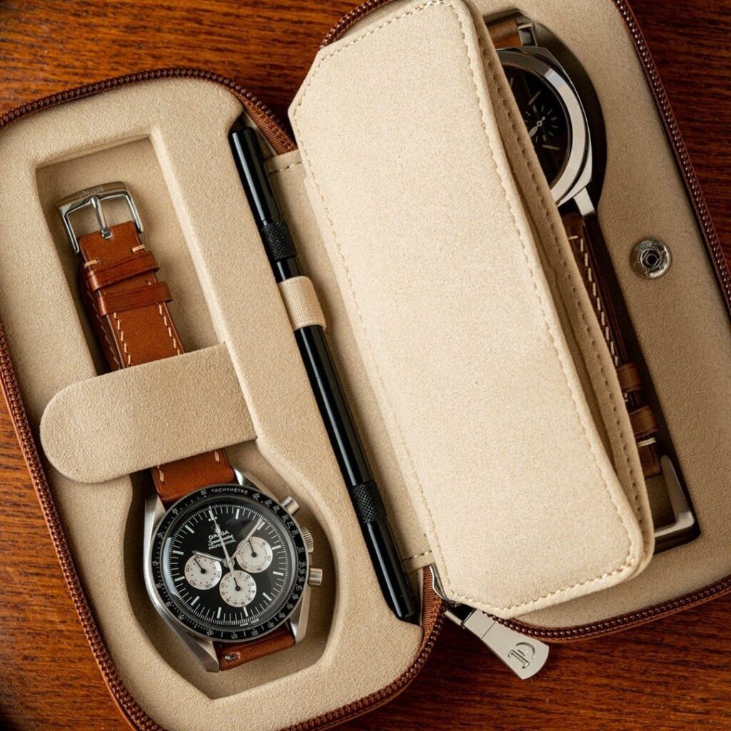 Leather watch case holding two wristwatches and a pen on a wooden table