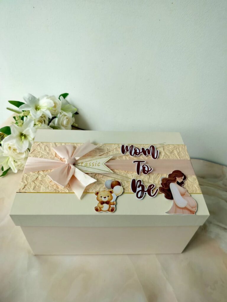 White gift box for a mother-to-be with pink bow and pregnancy decorations.