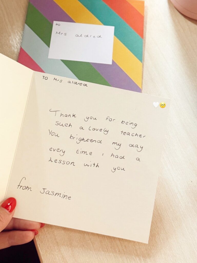 Handwritten thank you note to a teacher held open next to a striped envelope.