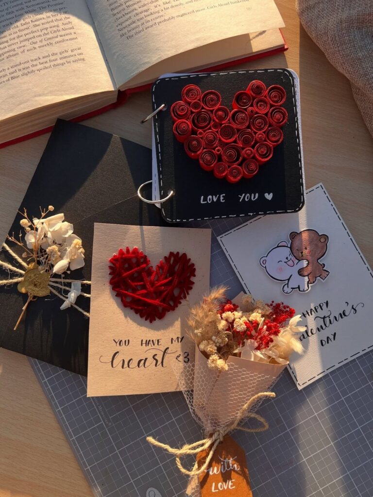 Handmade Valentine's Day gifts including a heart-decorated notebook, cards, and dried flowers.