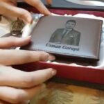 Brown leather wallet with engraved portrait and name inside a gift box.